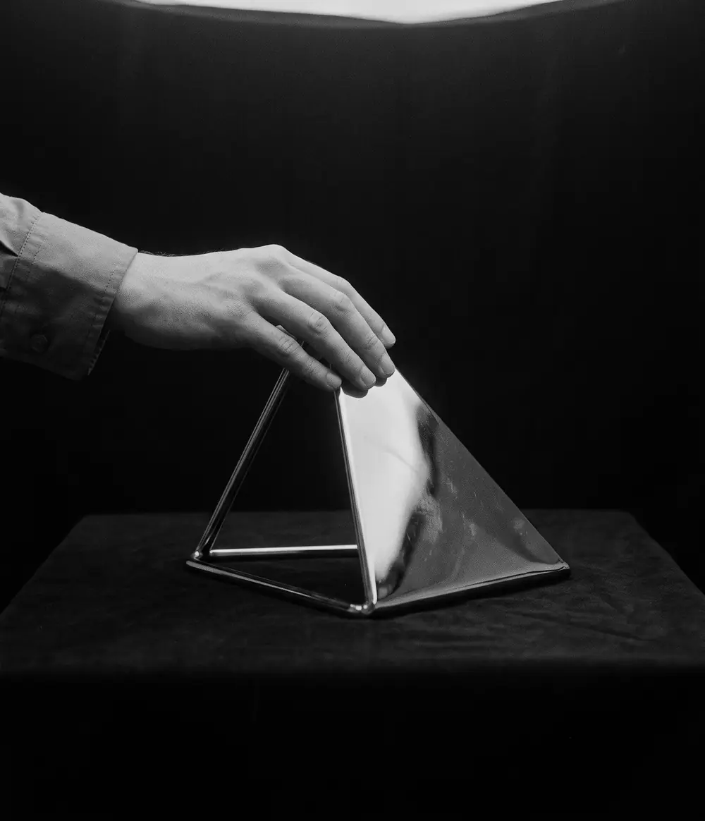 A hand resting on a polished chrome triangle under a single light